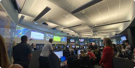 Large room full of people looking at big screens with information about the storm